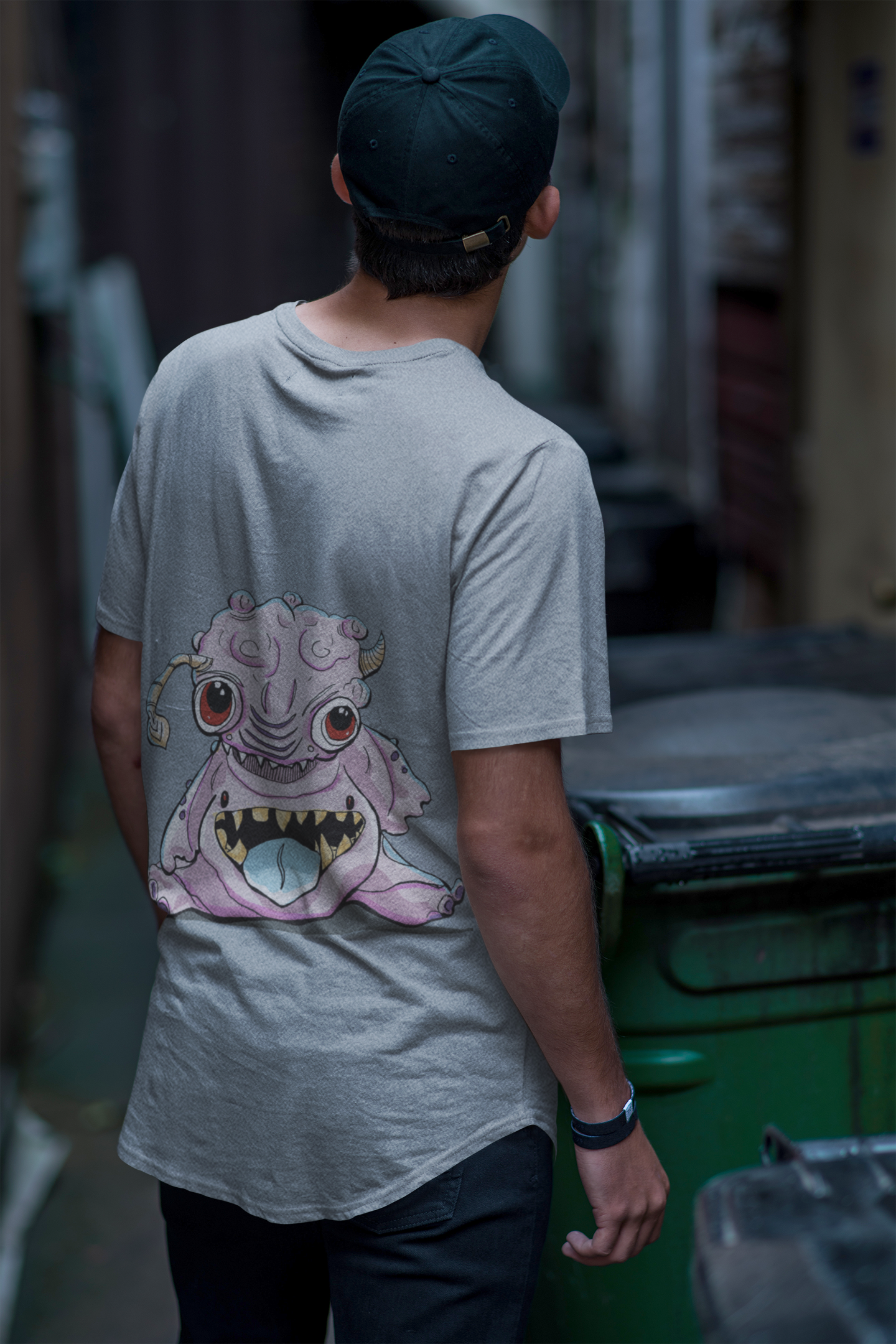 A man in a cap standing back towards camera in an alley in a pale blue shirt. With a pink bublegum looking alien creature on the back of the shirt